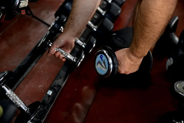 manos de un socio de Planet Vertical en Alcalá de Henares, cogiendo un par de pesas para la clase de fitness