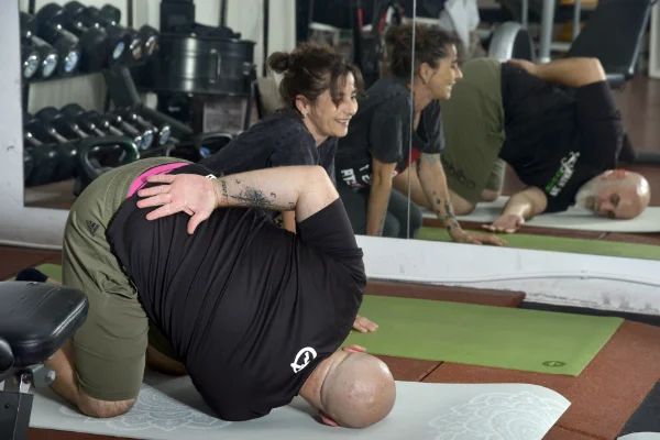 Raquel, monitora de Planet Vertical en Alcalá de Henares, sonriendo mientras revisa la posición de estiramiento de varios socios, con Edu, socio de Planet Vertical, delante de ella realizando la posición
